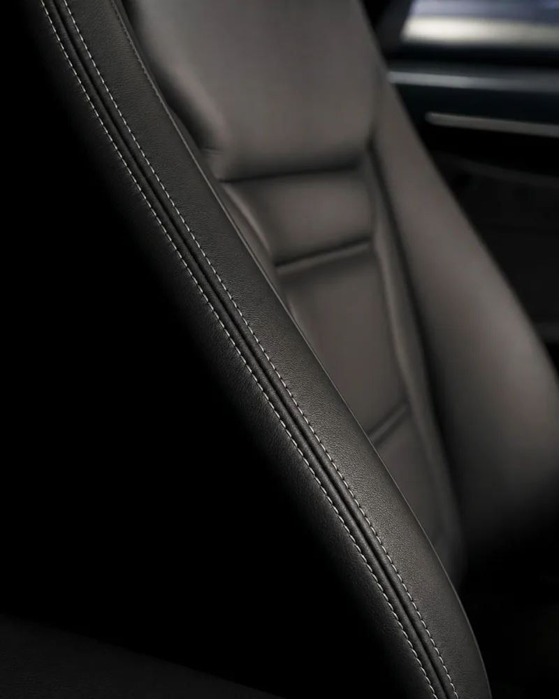 A black leather seat bolster with pale grey stitching, in side light.