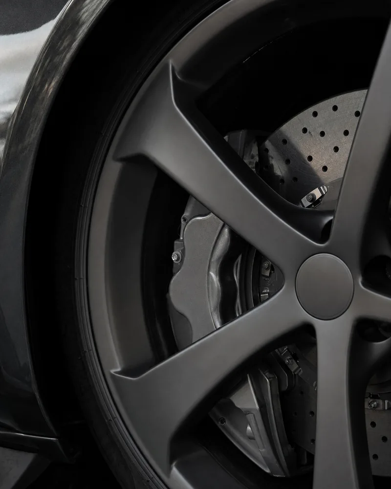 A brake caliper and a drilled disc behind the spokes of a dark alloy wheel.