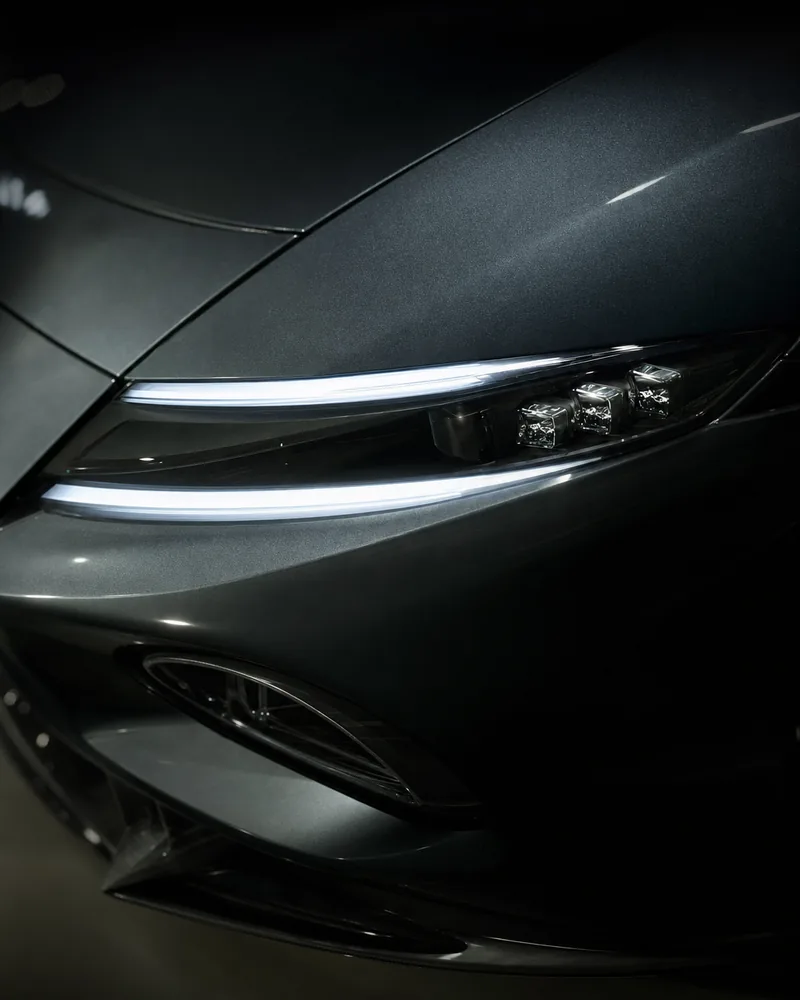A thin LED headlight signature, lit, set into graphite paint.